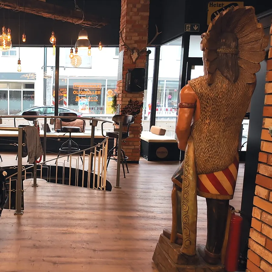 Vorderer Ladenbereich mit Barberstuhl, Werkzeugwagen, Wendeltreppe und einer großen geschnitzten Holzfigur vor dem Schaufenster