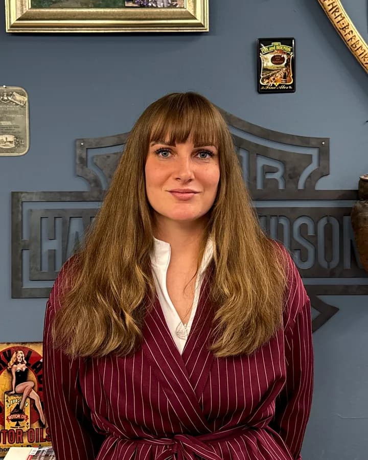 Lara, zuständig für Kosmetik, mit langen Haaren im dunkelroten Nadelstreifen-Outfit
